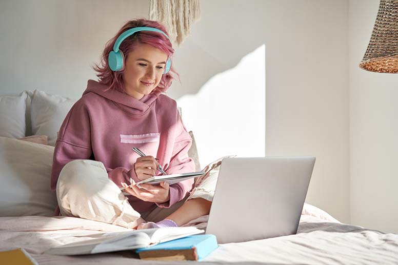 Tyttö istuu sängyllä ja käyttää tietokonetta