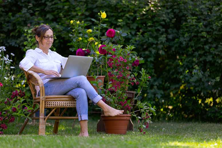 nainen istuu puutarhatuolissa ja tekee töitä tietokoneella