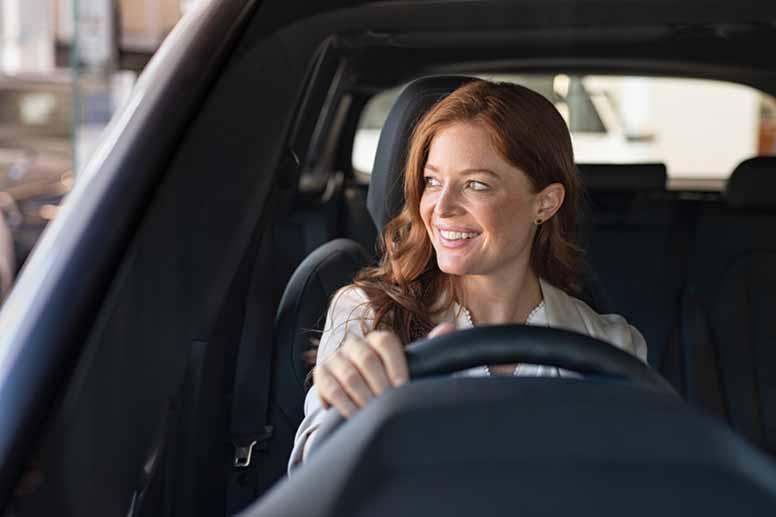 Hymyilevä nuori nainen ajaa uutta autoa