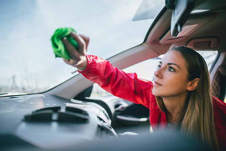 Nainen puhdistaa auton tuulilasia