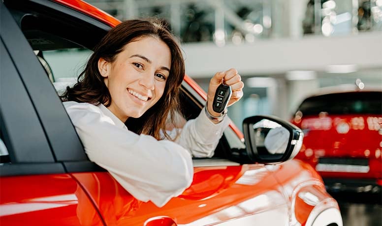 Nainen istuu punaisessa autossa, kädessä on autonavain