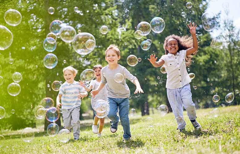Lapset juoksetvat nurmikolla ja  pyydystävät saippuakuplia