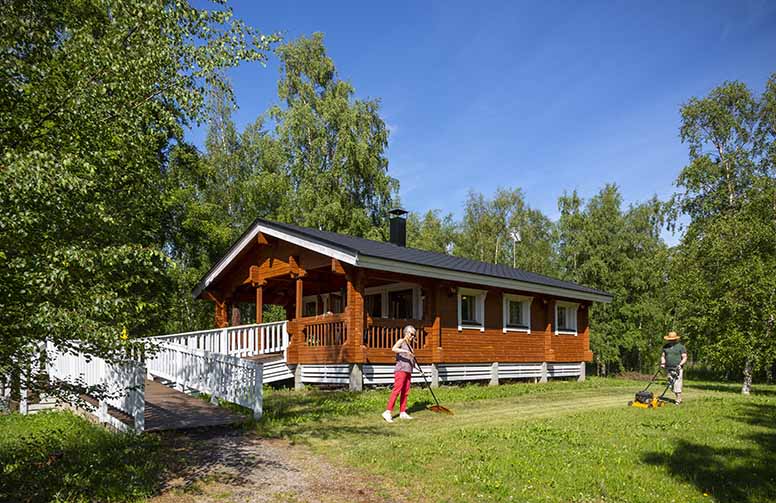 Nainen haravoi pihaa ja mies leikkaa ruohoa kesämäkillä