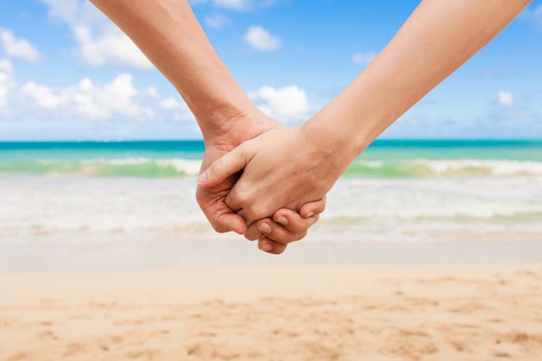 Pariskunta kävelee käsikädessä aurinkoisella uimarannalla