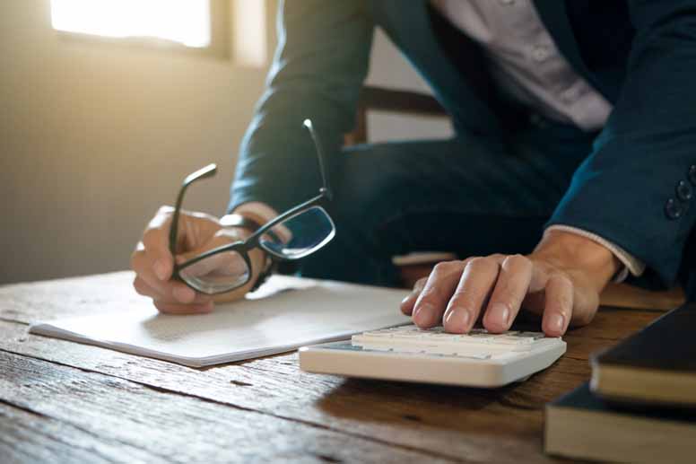 Mies tarkastelee papereita ja käyttää laskinta
