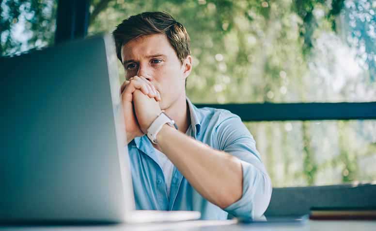 Nuori mies katselee kannettavaa tietokonetta huolestuneena