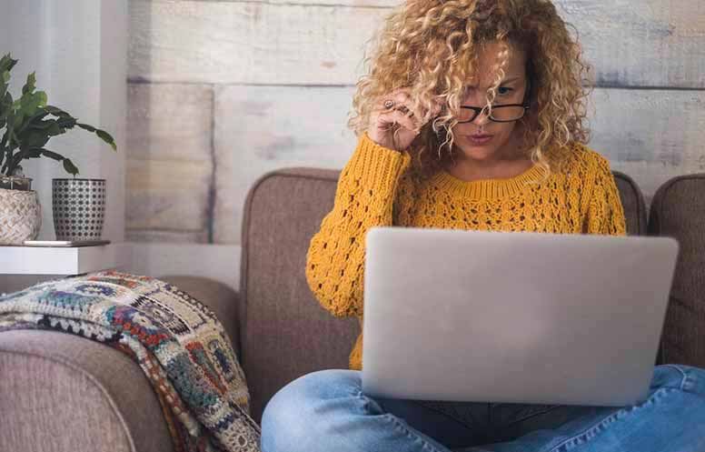 nainen istuu sohvalla ja katselee kannettavaa tietokonetta