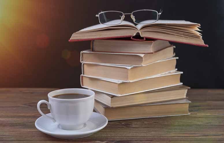 Kirjoja, kahvikuppi ja silmälasit