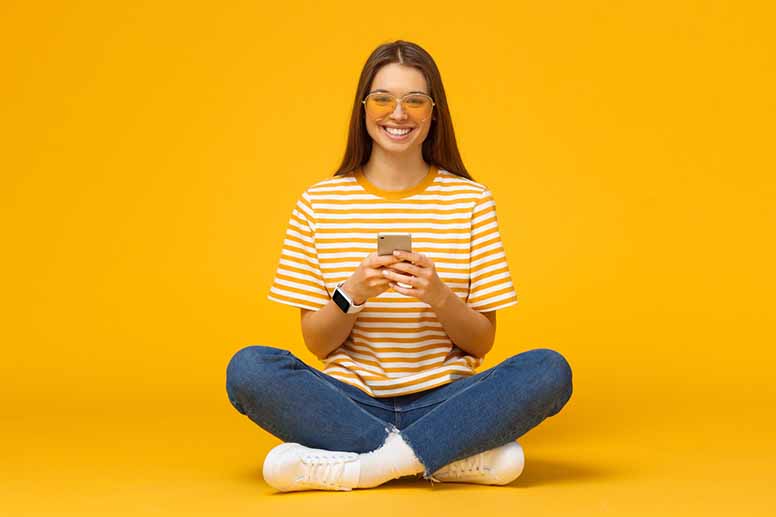 Nuori nainen hymyilee aurinkolasit silmillä, kädessä on älypuhelin