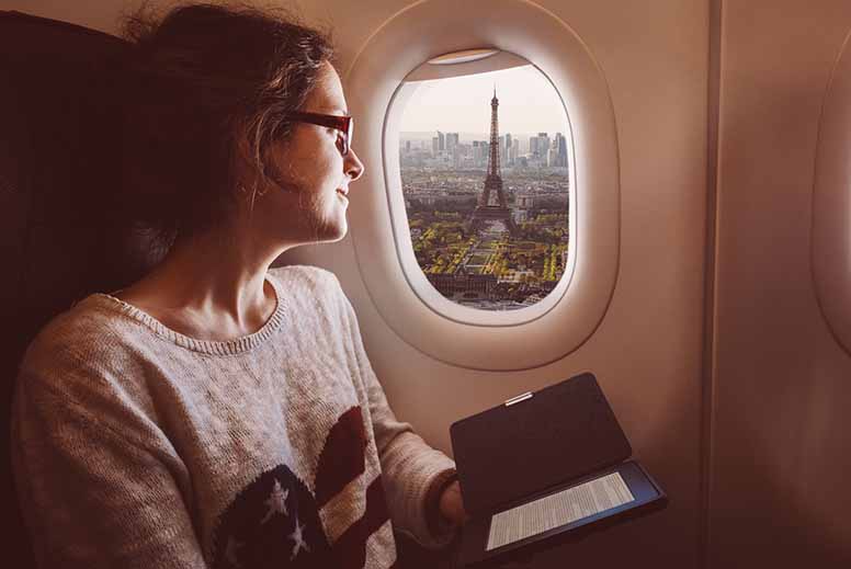 Nainen istuu lentokoneessa ja lukee e-kirjaa.