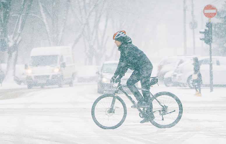 Mies pyöräilee lumituiskussa