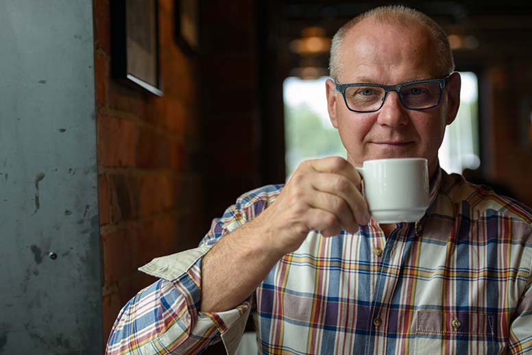 Mies juo kahvia, päässä on silmälasit ja päällä on ruutupaita