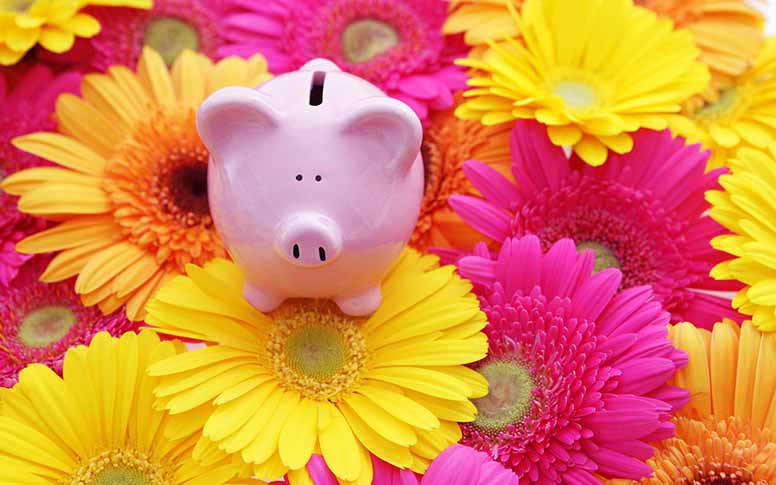 Säästöpossu keltaisten ja pinkkien kukkien keskellä