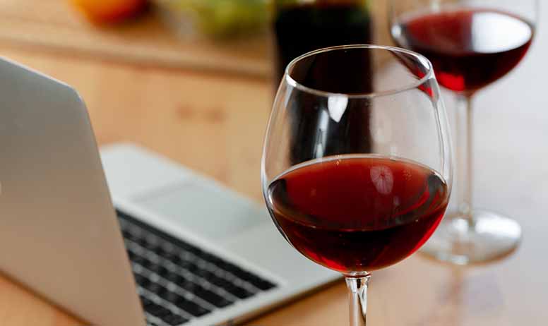 Kannettava tietokone ja kaksi lasia punaviiniä