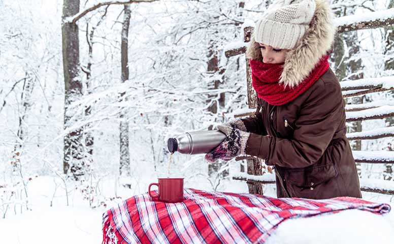 Nainen kaataa teetä termospullosta mukiin 